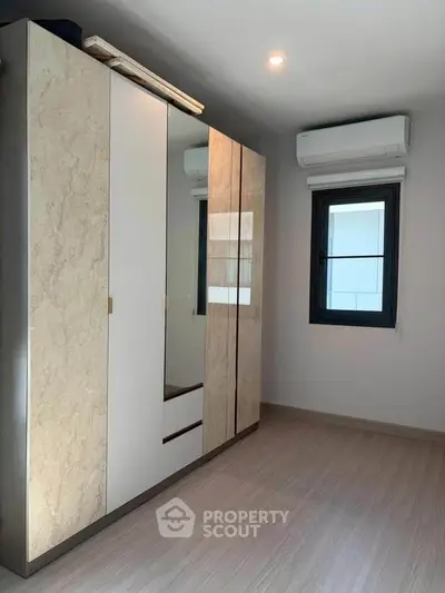Modern bedroom with sleek wardrobe and air conditioning unit, featuring minimalist design and natural light.