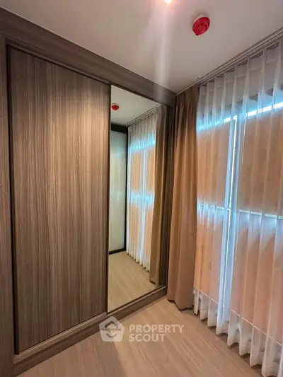 Spacious bedroom with elegant wooden wardrobe and large windows with sheer curtains.