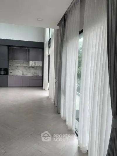 Spacious modern living room with floor-to-ceiling windows and elegant curtains, featuring a sleek open kitchen.