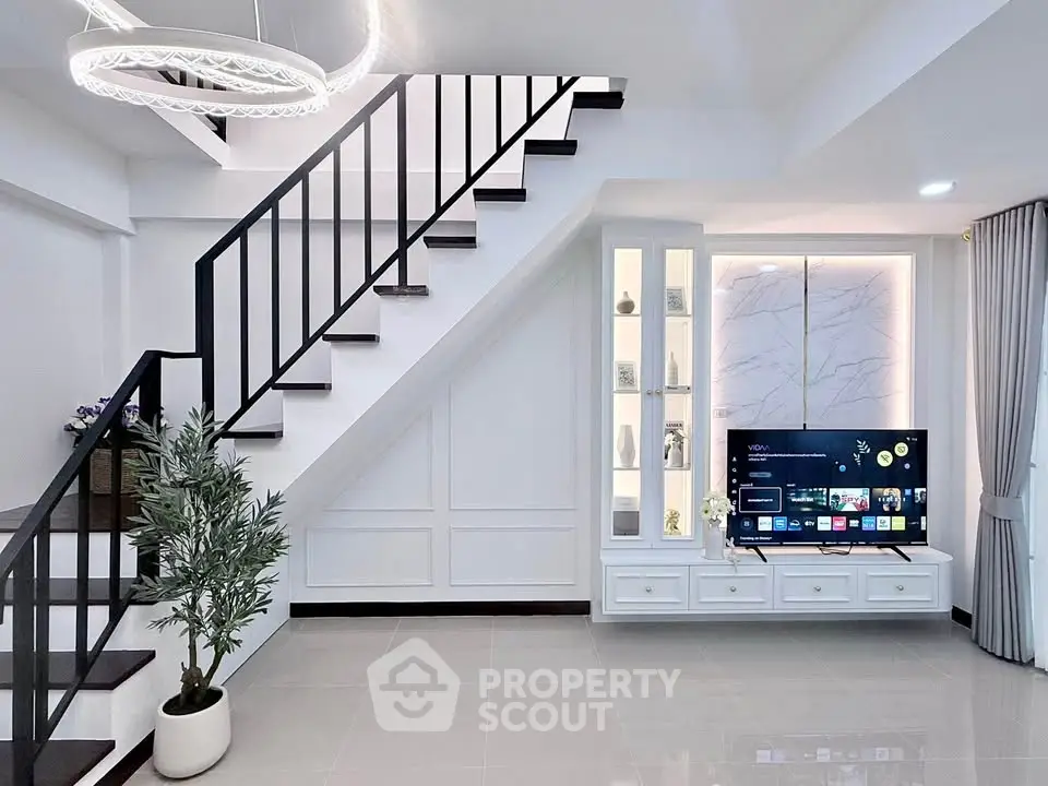 Modern living room with sleek staircase and built-in TV unit, featuring elegant lighting and minimalist decor.