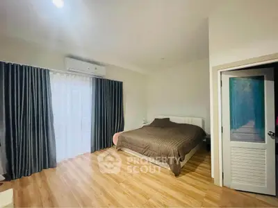Spacious bedroom with wooden flooring and large window, featuring modern decor and ample natural light.