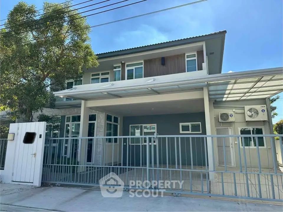 Modern two-story house with gated entrance and carport, featuring sleek design and spacious outdoor area.