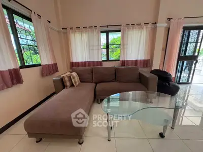 Spacious living room with stylish L-shaped sofa and glass coffee table, featuring large windows and elegant curtains.