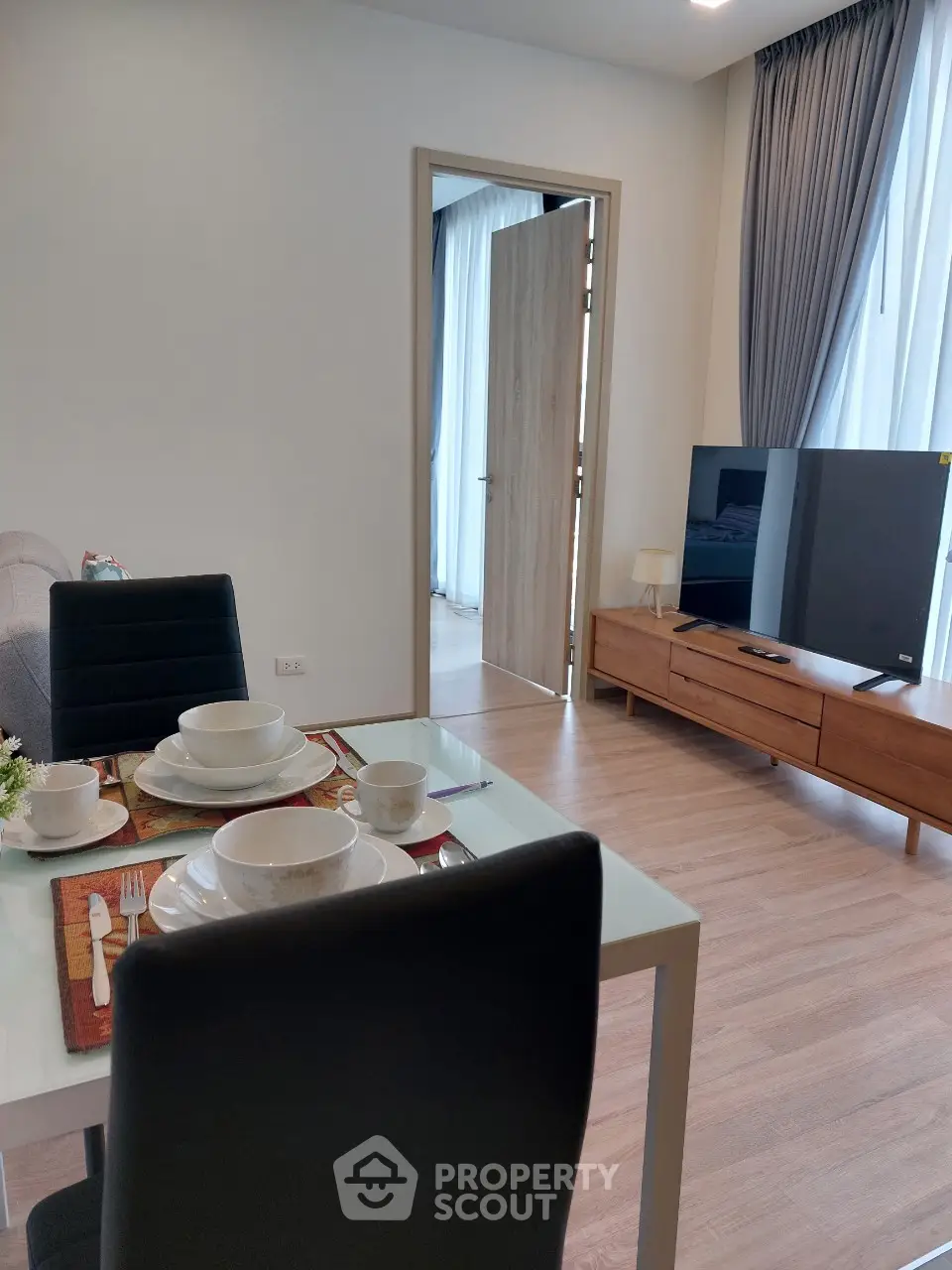 Modern living room with dining area and TV, featuring elegant decor and natural light.