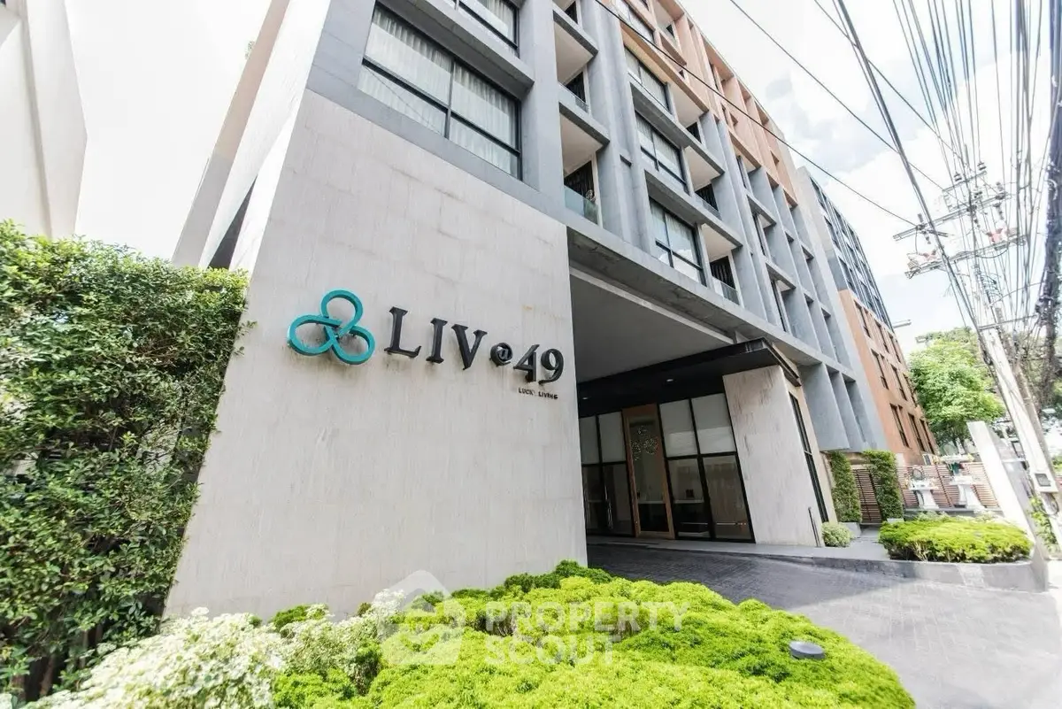 Modern apartment building entrance with lush greenery and sleek architectural design.