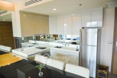 Modern kitchen with sleek cabinetry, stainless steel fridge, and elegant dining area in a stylish apartment.