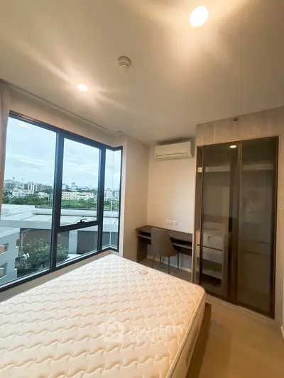 Modern bedroom with large window offering city view, featuring a comfortable bed and a sleek study area.