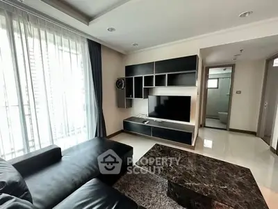 Modern living room with sleek black furniture and large TV unit, featuring natural light from large windows.