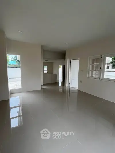 Spacious empty living room with glossy tiled floors and large windows in modern home.