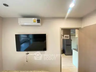 Modern apartment interior with wall-mounted TV and air conditioning, leading to a sleek kitchen area.