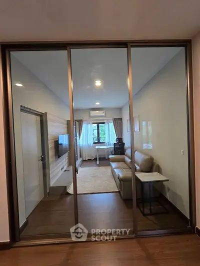 Modern living room with glass partition, cozy seating, and natural light.