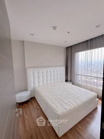 Spacious bedroom with large window offering stunning city views, featuring a modern white bed and wooden flooring.