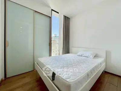 Modern bedroom with minimalist design and large window offering city view.