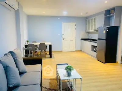 Modern open-layout living room with kitchen, featuring sleek furniture and wooden flooring.