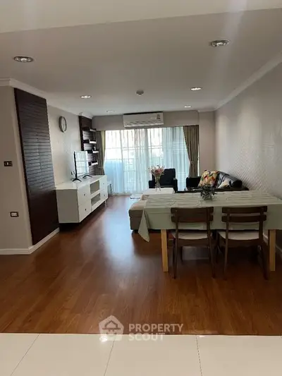 Spacious living room with modern decor and wooden flooring, featuring a cozy dining area and large windows.