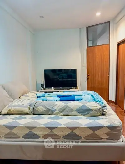 Spacious bedroom with modern decor and large TV, perfect for relaxation.