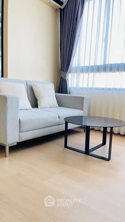 Modern living room with stylish sofa and coffee table, featuring large window with elegant curtains.