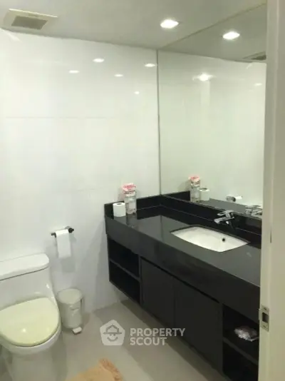 Modern bathroom with sleek black countertop and large mirror in a contemporary apartment.