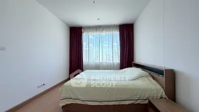 Spacious bedroom with large window and modern furnishings in a high-rise apartment.