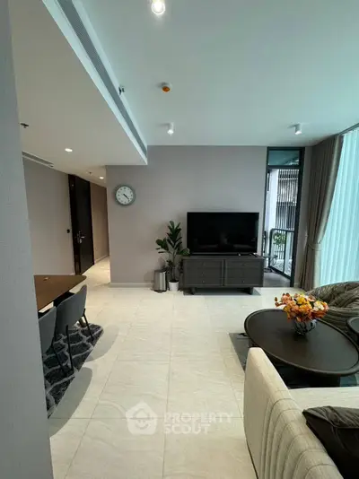 Modern living room with sleek furniture and natural light, featuring a TV and elegant decor.