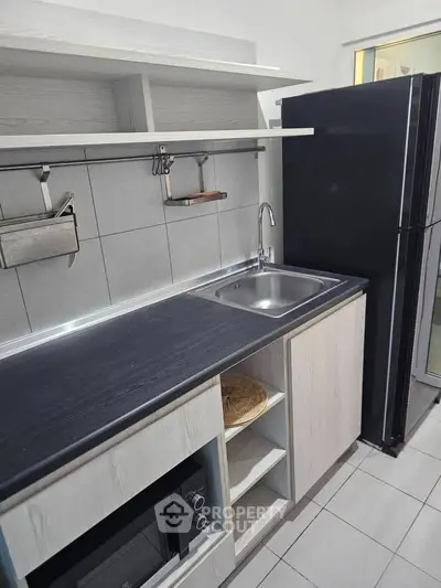 Modern kitchen with sleek black countertop and stainless steel sink, featuring a microwave and spacious fridge.