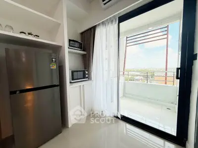 Modern kitchen with stainless steel fridge and microwave, leading to a bright balcony with city views.