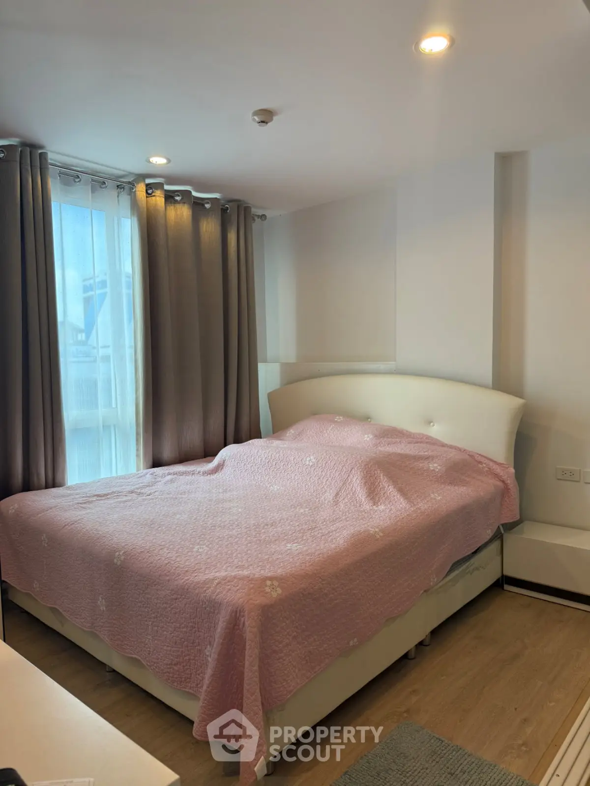 Cozy bedroom with large window and elegant curtains, featuring a comfortable bed with a pink quilt.