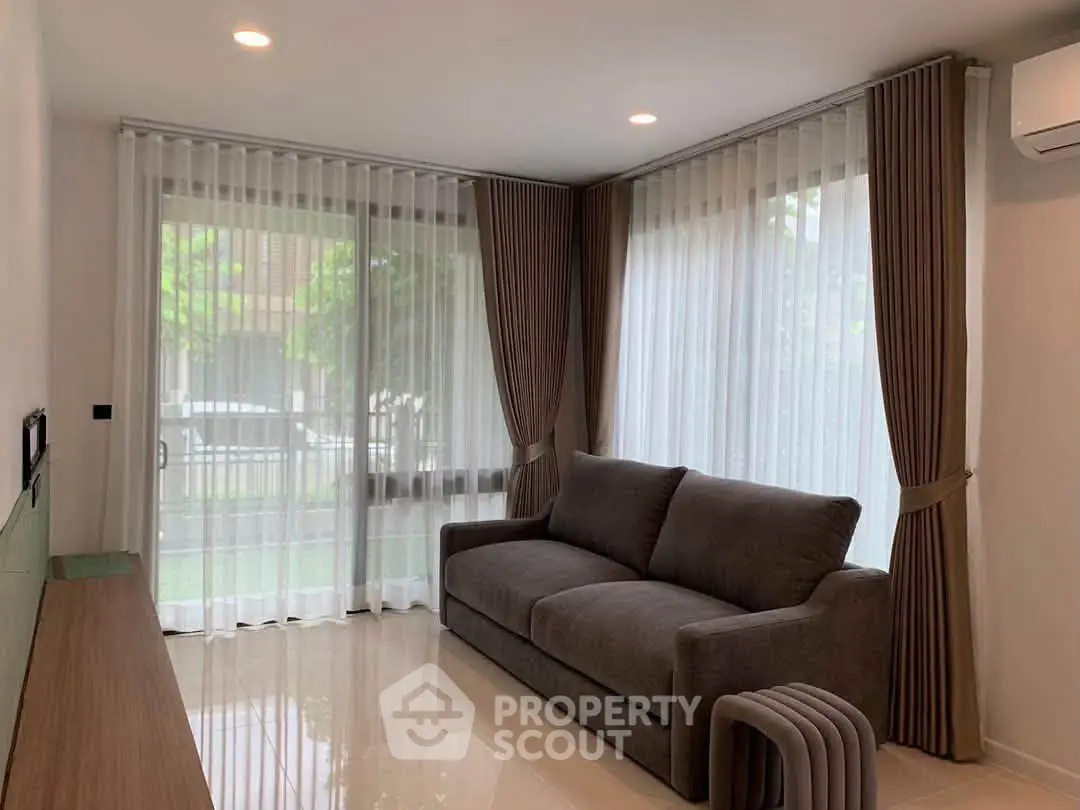 Modern living room with large windows and elegant curtains, featuring a comfortable gray sofa and sleek decor.