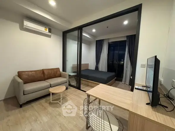 Modern studio apartment with cozy living area and bedroom separated by glass partition.