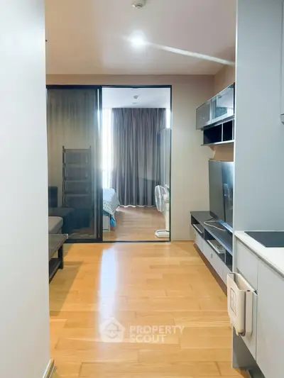 Modern apartment interior with wooden flooring and glass partition leading to bedroom.