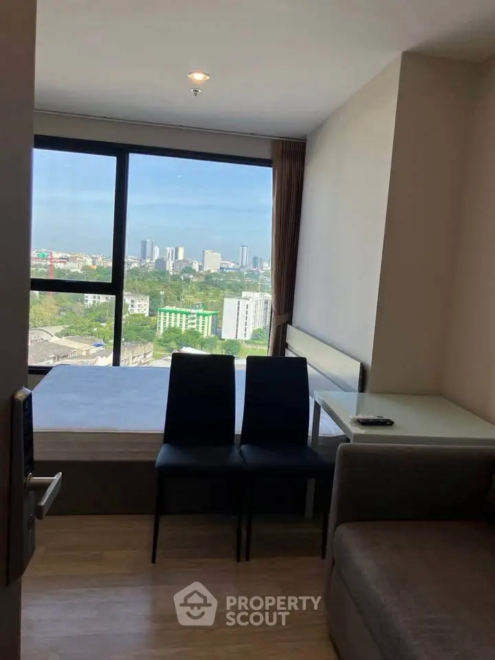 Modern apartment with stunning city view from large window, cozy seating area, and sleek furnishings.