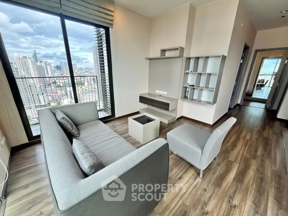 Modern living room with city view, featuring sleek furniture and large windows in a high-rise apartment.