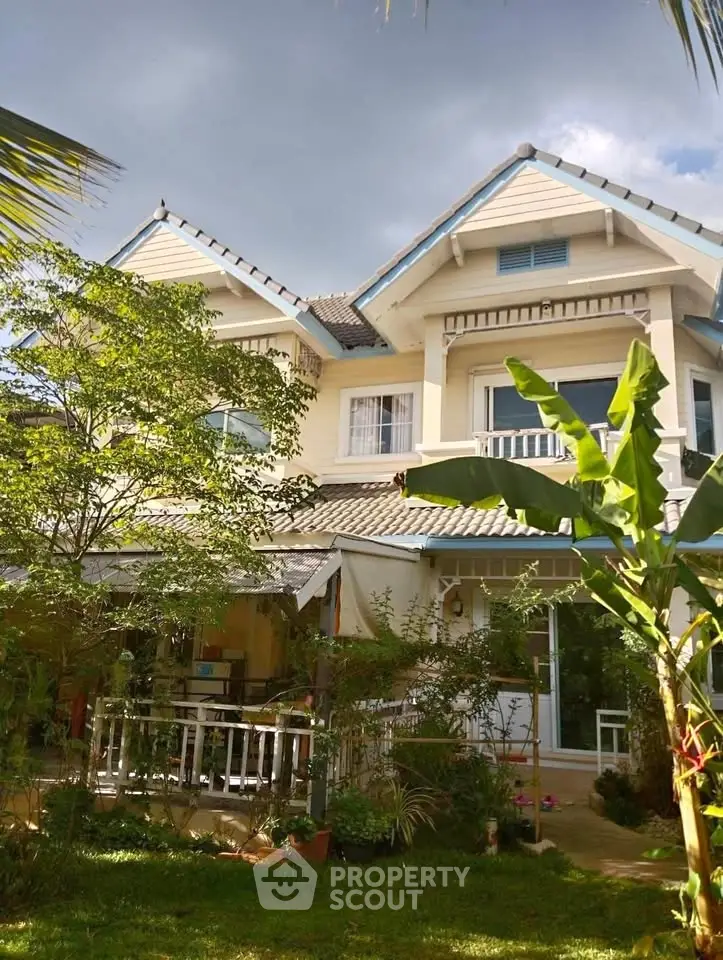 Charming two-story house with lush garden and inviting porch under a cloudy sky.