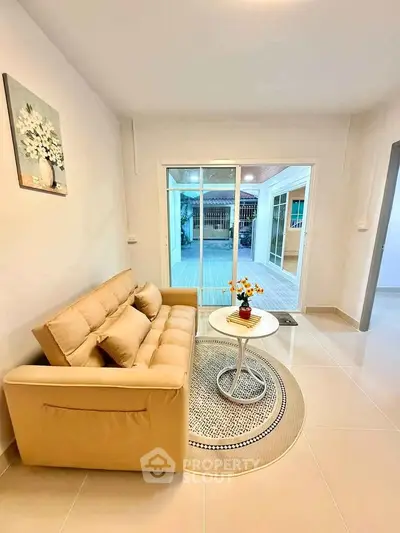 Cozy living room with beige sofa and round table, opening to a bright patio area.