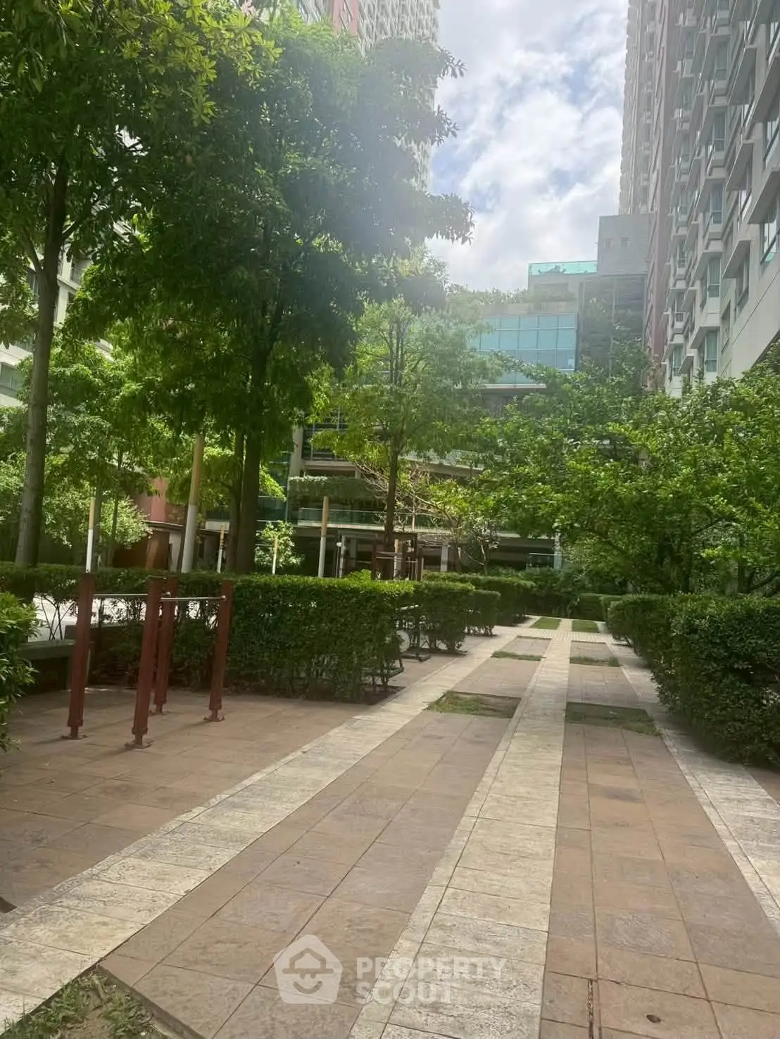 Lush garden pathway in modern residential complex with tall buildings and greenery.