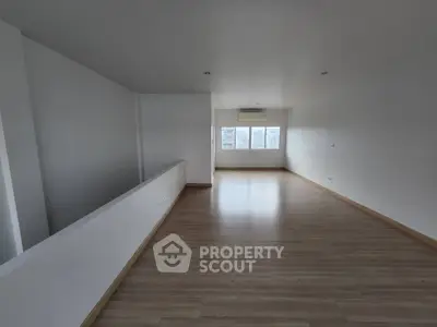 Spacious empty room with wooden flooring and large windows offering natural light.