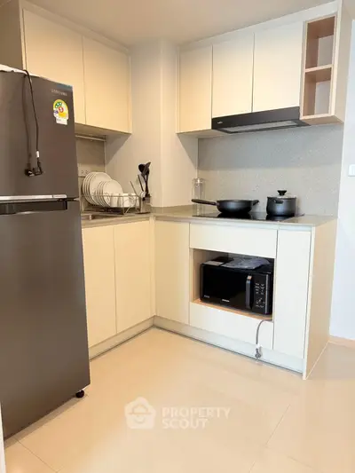 Modern kitchen with sleek cabinets, stainless steel fridge, and built-in microwave in a cozy apartment.