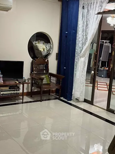 Elegant living room with polished floors, vintage chair, and modern TV setup, leading to a stylish wardrobe area.