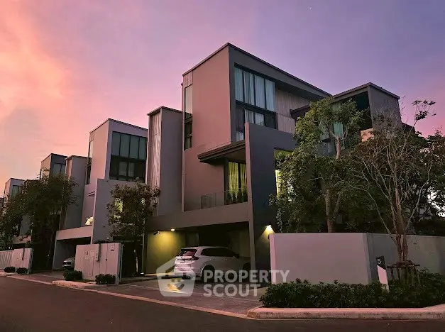 Modern townhouse complex at sunset with sleek design and lush greenery.