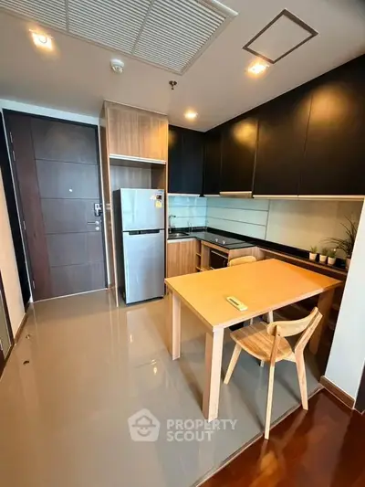 Modern kitchen with sleek cabinets, stainless steel fridge, and wooden dining set in a stylish apartment.