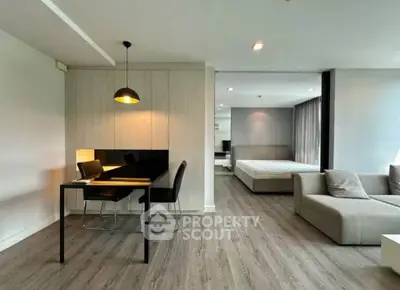 Modern open-plan living room with dining area and bedroom, featuring sleek furniture and large windows.