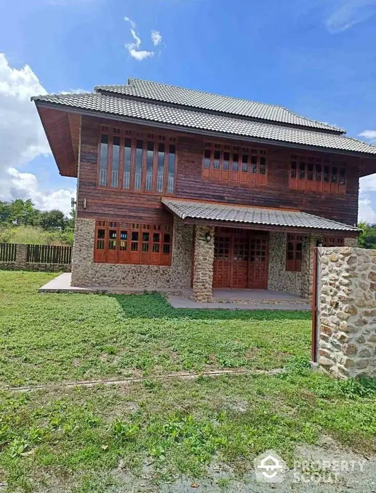 Charming rustic two-story house with stone and wood exterior, surrounded by lush greenery.