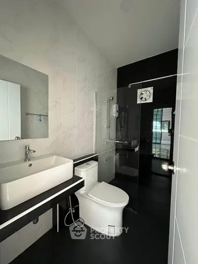 Modern bathroom with sleek black and white design, featuring a spacious shower and contemporary fixtures.