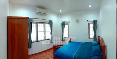 Cozy bedroom with wooden furniture and blue bedding, featuring natural light from large windows.