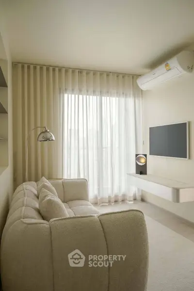 Modern living room with cozy sofa, wall-mounted TV, and large window with sheer curtains.