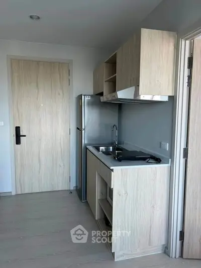 Modern compact kitchen with sleek wooden cabinets and stainless steel appliances in a stylish apartment.
