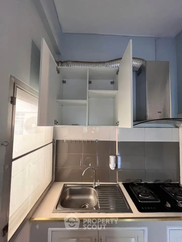 Compact kitchen with gas stove and overhead cabinets in modern apartment