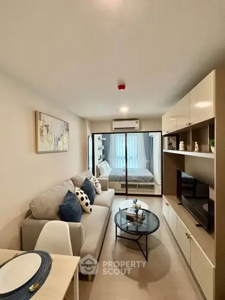 Modern living room with cozy sofa and stylish decor leading to a bright bedroom with large windows.