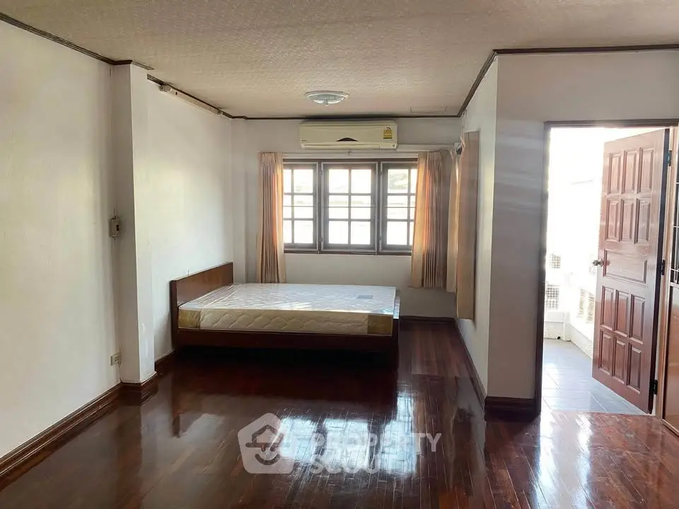 Spacious bedroom with wooden floors and natural light in a modern apartment.