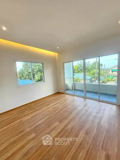 Spacious living room with wooden flooring and large windows opening to a balcony with scenic views.